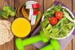Mesa com alimentos e objetos que representam a perda de peso, como verduras, saladas, halteres e uma fita métrica.