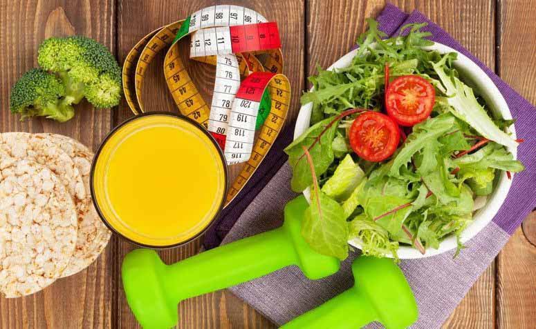 Mesa com alimentos e objetos que representam a perda de peso, como verduras, saladas, halteres e uma fita métrica.