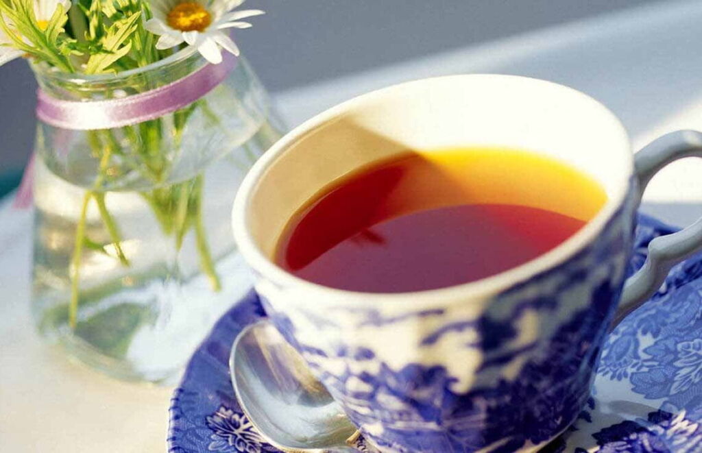 Mesa com xícara e pires com chá de hibisco e um vaso transparente com água e flores.