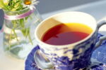 Mesa com xícara e pires com chá de hibisco e um vaso transparente com água e flores.
