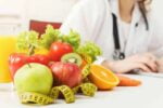 Sala de uma nutricionista que está sentada em sua mesa com seus equipamento e alimentos saudáveis.