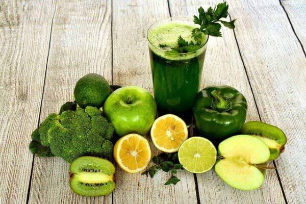 Mesa com alimentos verdes, como frutas e verduras, e um copo de vidro com o suco verde detox.