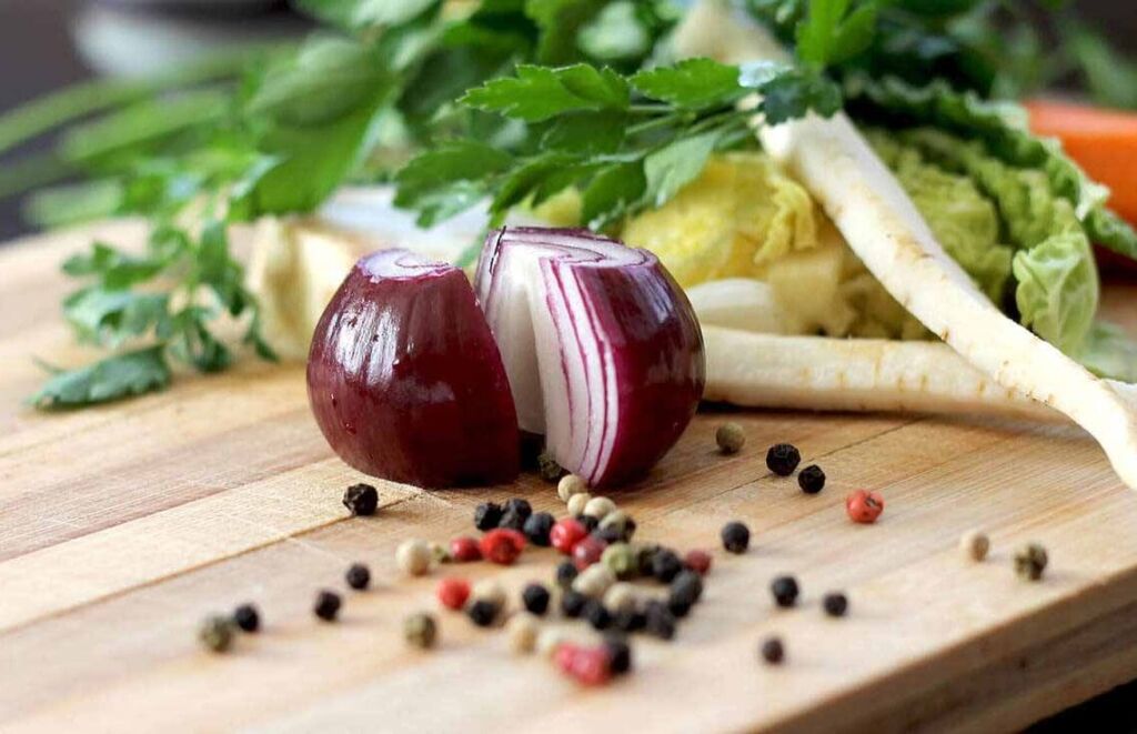 Mesa com tábua de madeira com alimentos que são aliados do emagrecimento, como cebola roxa e verduras.