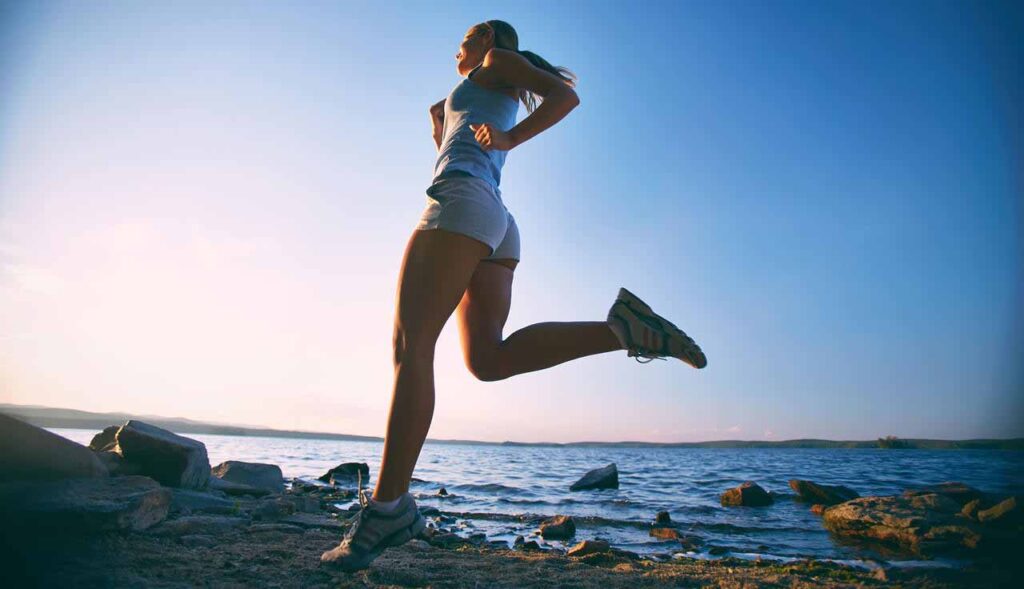 Mulher se exercitando enquanto corre em uma praia no final da tarde.