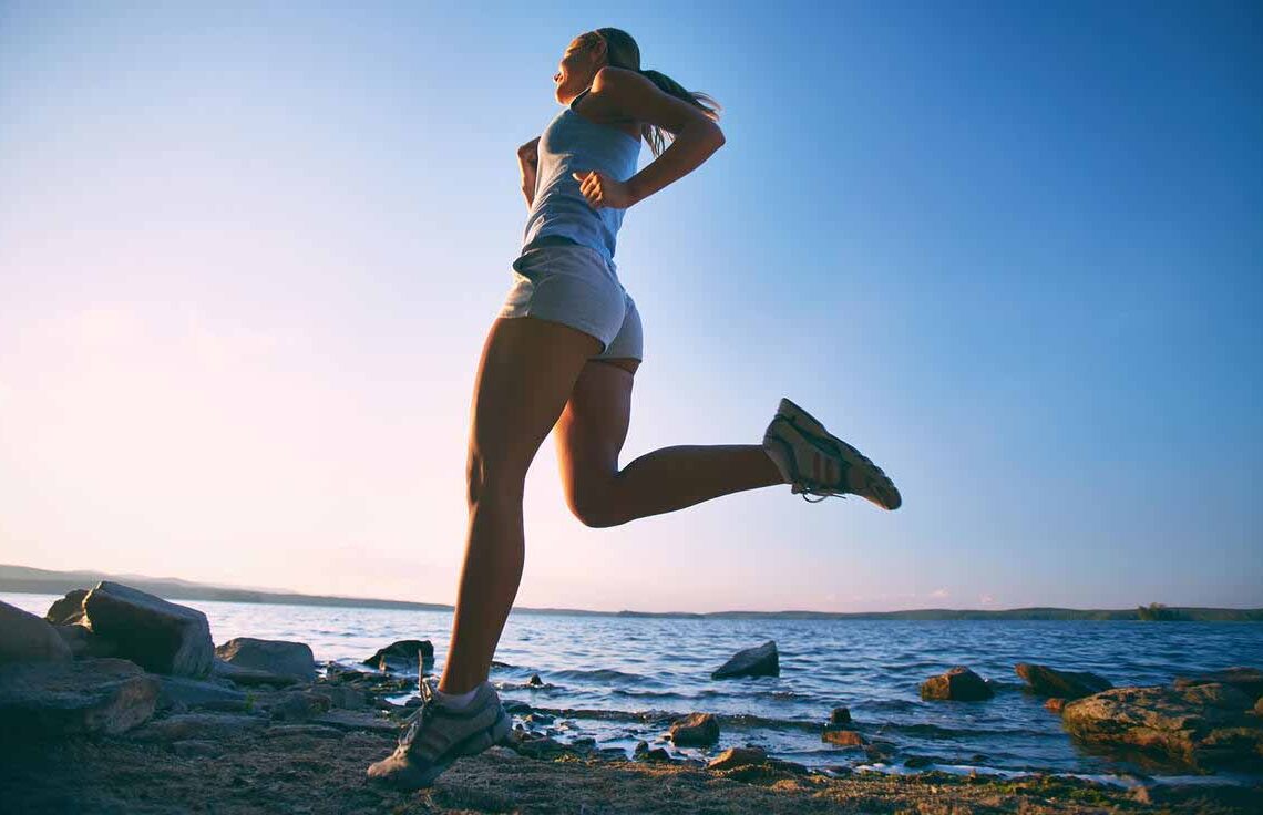 Mulher se exercitando enquanto corre em uma praia no final da tarde.