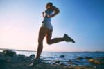 Mulher se exercitando enquanto corre em uma praia no final da tarde.