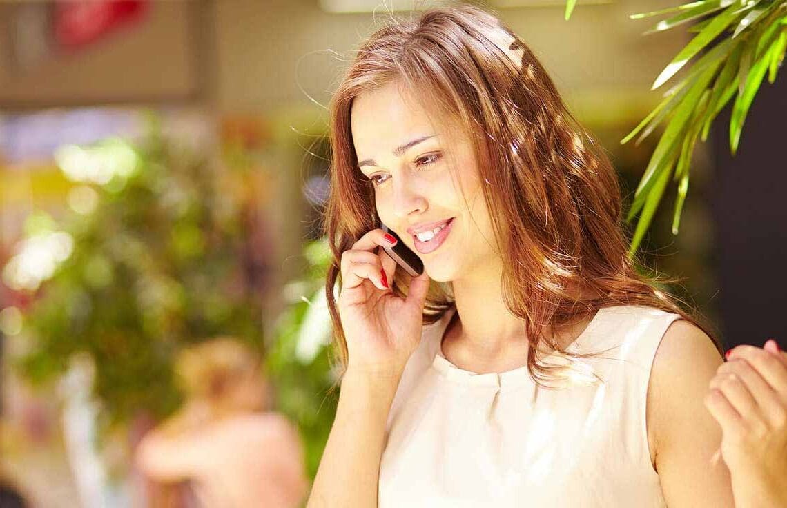 Mulher sorrindo em uma área externa arborizada enquanto fala ao celular.