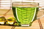Xicara de vidro em uma mesa com chá verde dentro.