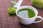 Mesa com xícara branca com green tea e colher branca com o pó do chá verde.