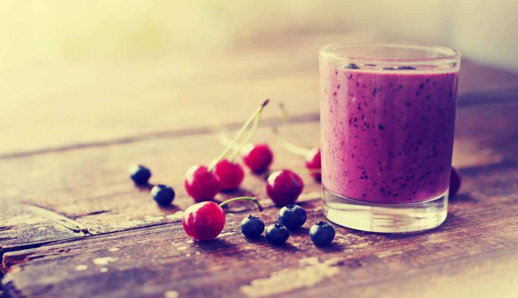 Mesa com um copo de suco de frutas vermelhas e frutinhas, representando os alimentos antioxidantes.
