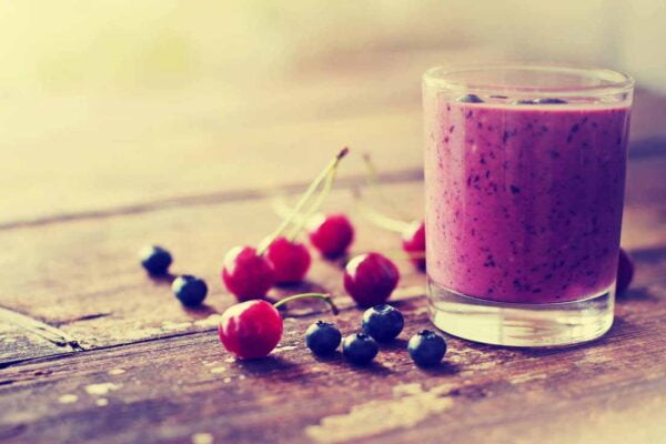 Mesa com um copo de suco de frutas vermelhas e frutinhas, representando os alimentos antioxidantes.