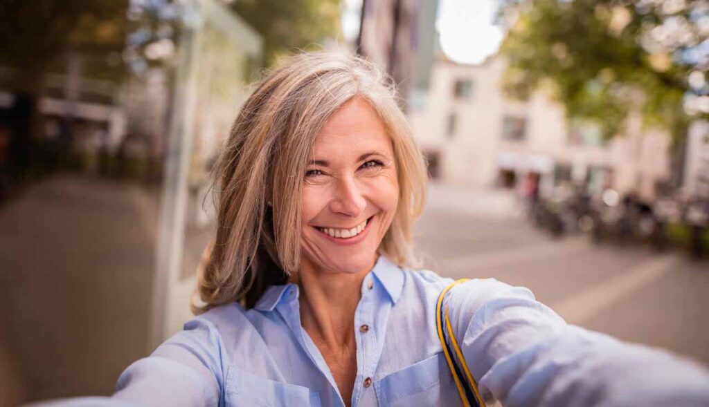 Mulher idosa sorrindo enquanto tira uma selfie na rua.