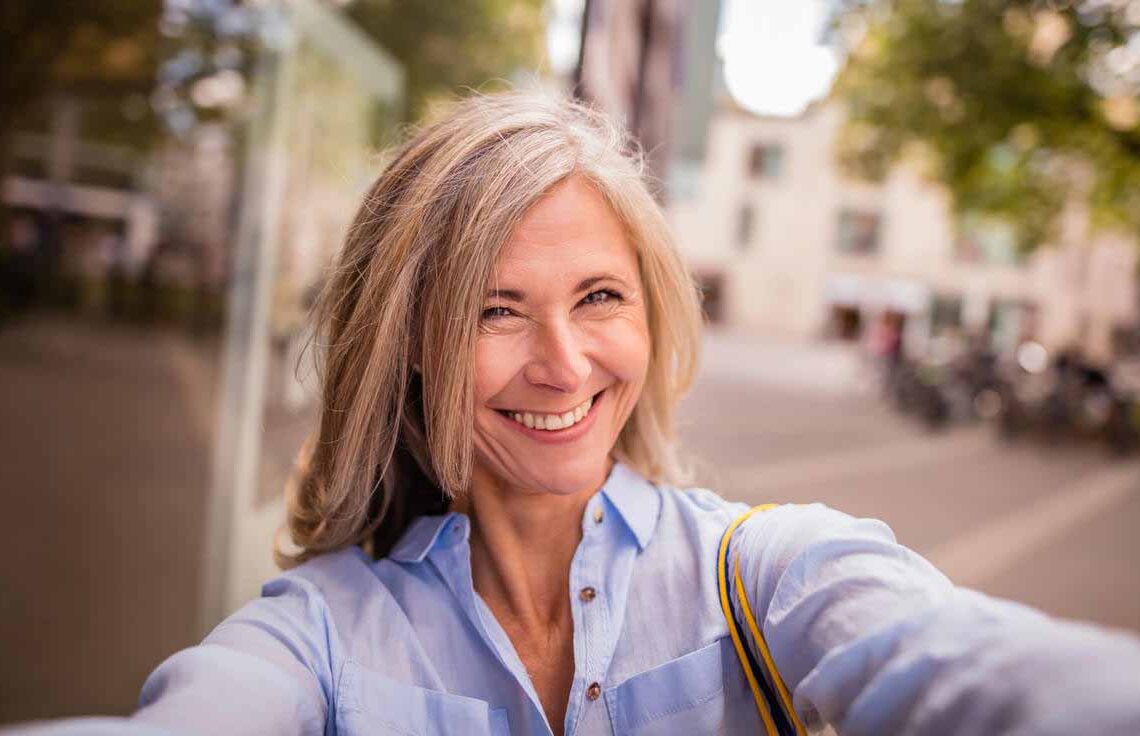 Mulher idosa sorrindo enquanto tira uma selfie na rua.