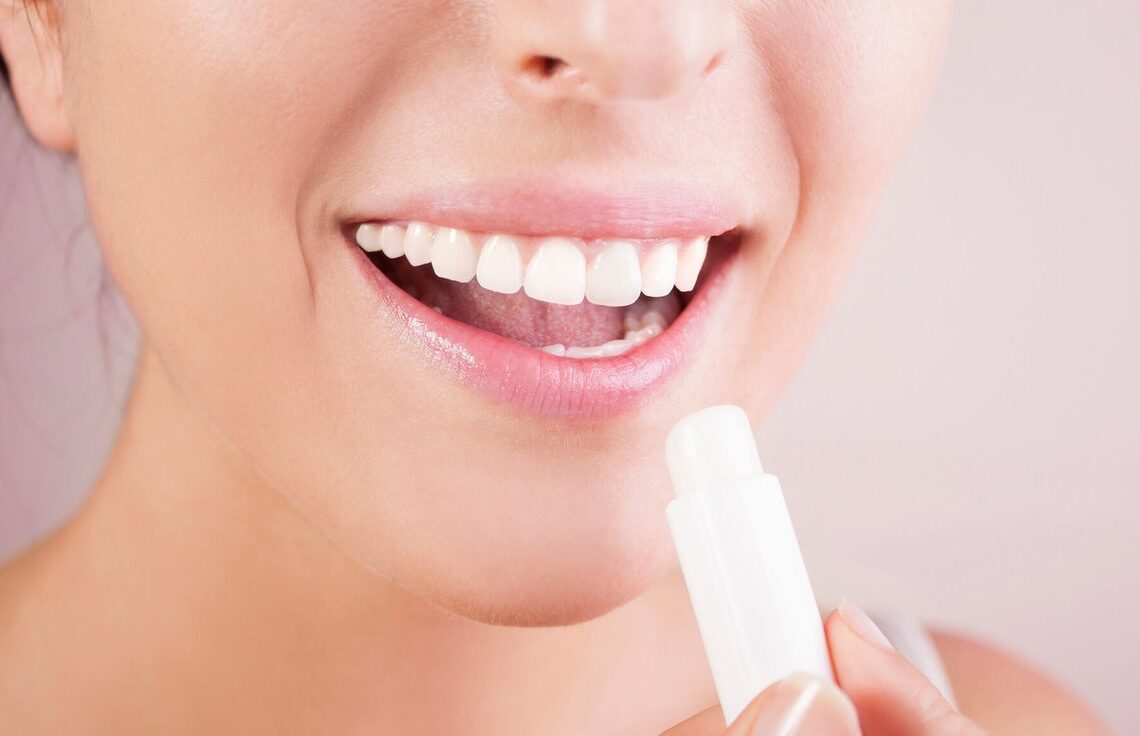 Mulher sorrindo enquanto hidrata seus lábios com um hidratante labial.