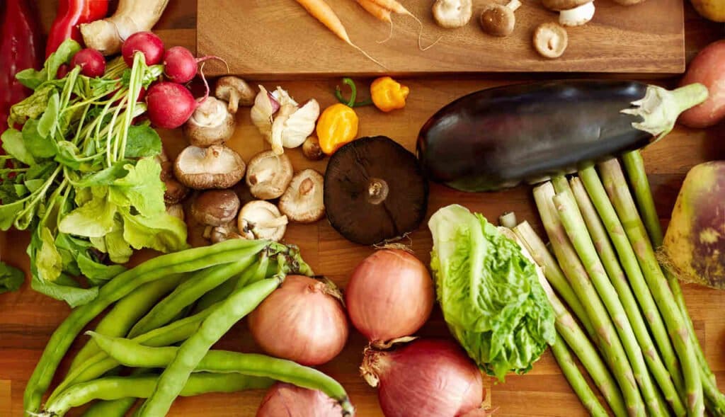 Mesa de madeira com várias opções de alimentos que ajudam na digestão, como legumes, verduras e cogumelos.