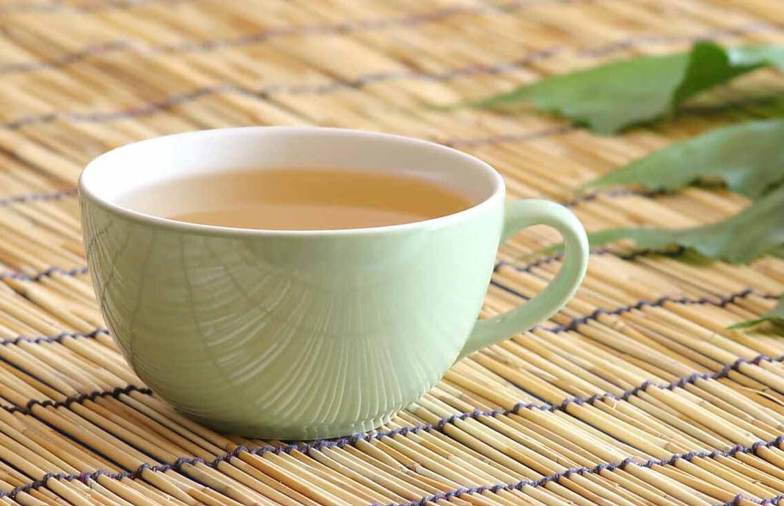Mesa com sousplat de madeira com uma xícara verde clara com o chá branco.