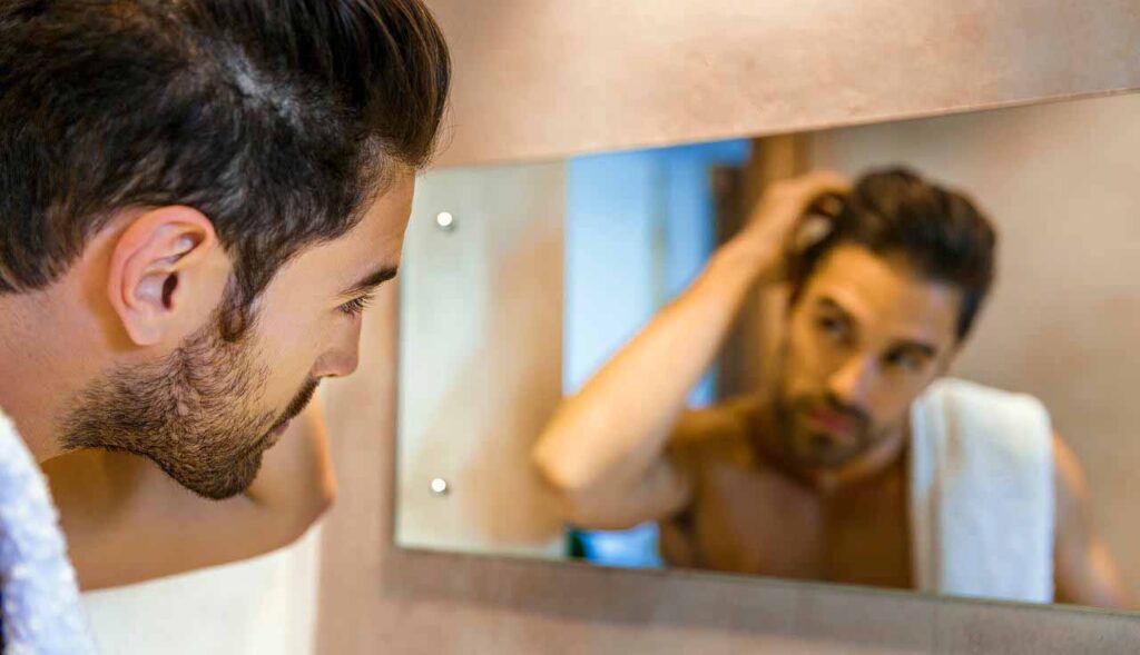 Homem conferindo seu cabelo no espelho do banheiro após iniciar uma alimentação para prevenir a caspa.