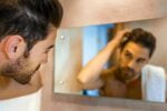Homem conferindo seu cabelo no espelho do banheiro após iniciar uma alimentação para prevenir a caspa.