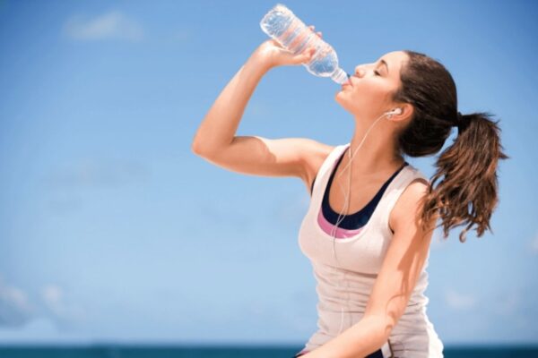 Mulher descansando após o treino ao ar livre, enquanto bebe uma garrafa de água.