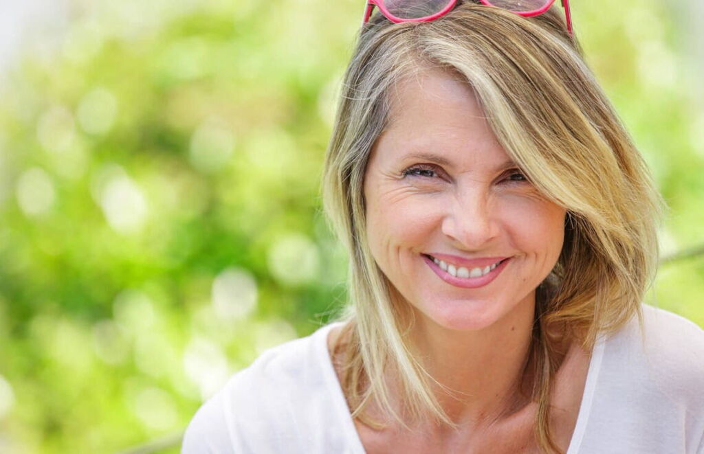 Mulher loira sorrindo com com um óculos rosa na cabeça.