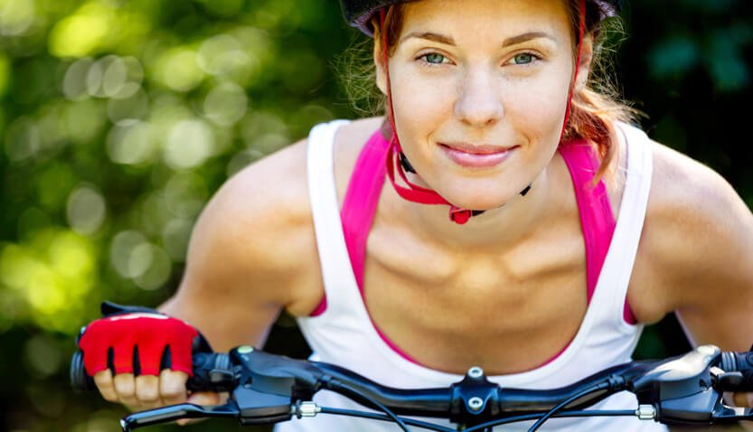 Mulher se exercitando no verão andando de bicicleta com luvas e capacete.