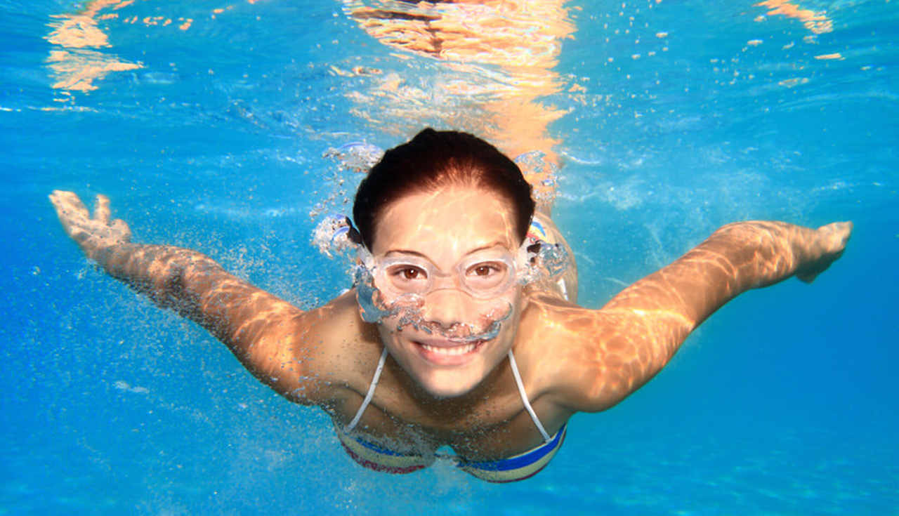 Mulher sorrindo nadando em uma piscina com oculos de natação.