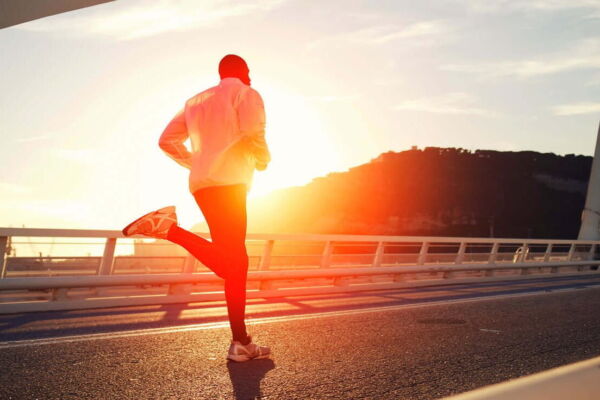 Homem se exercitando correndo em uma rua ao pôr do sol.