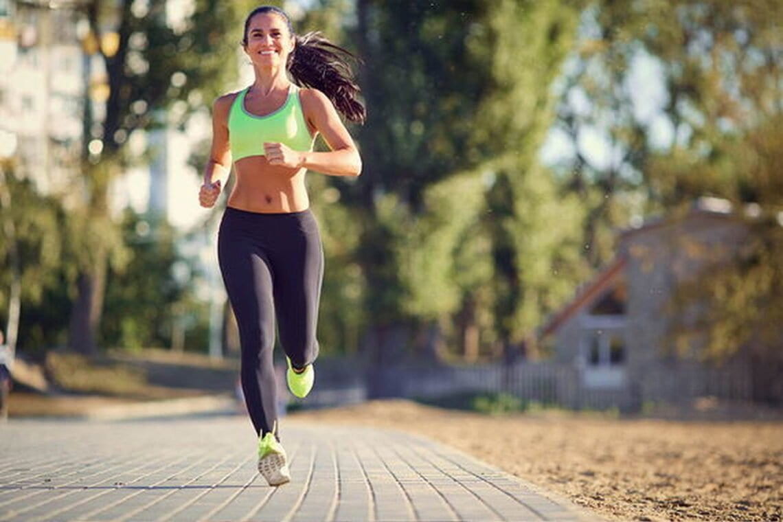 Mulher sorrindo enquanto se exercita correndo em uma rua.
