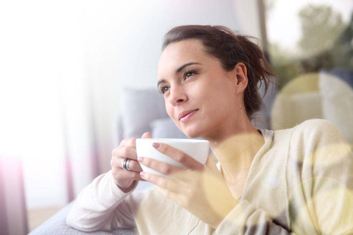 Mulher relaxando em sua casa enquanto toma seu chá funcional em uma xícara.