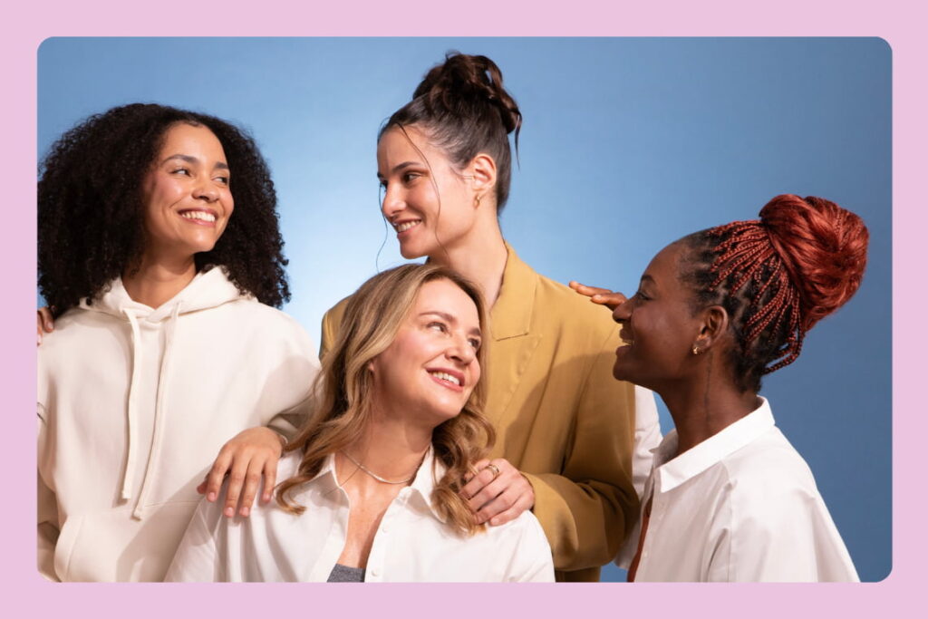 Quatro mulheres sorrindo e interagindo juntas contra fundo azul.
