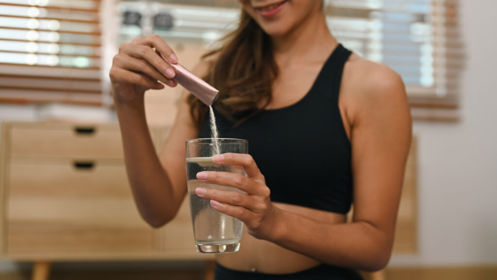 Mulher colocando colágeno hidrolisado em um copo com água