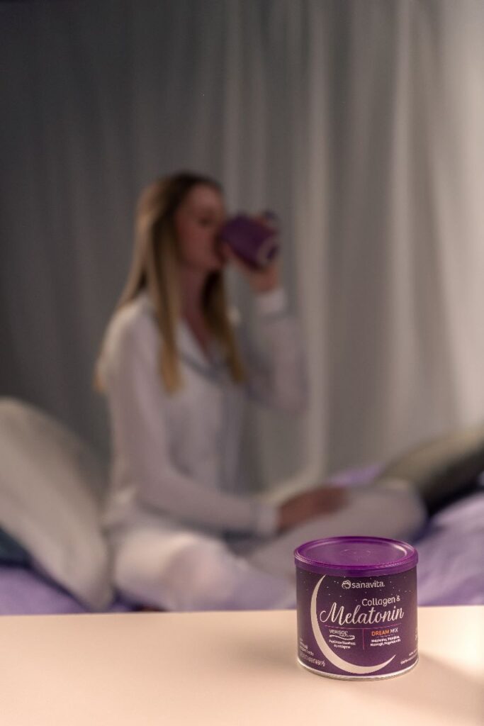 Mulher de pijama sentada na cama tomando sua xícara de Collagen e Melatonin Sanavita 