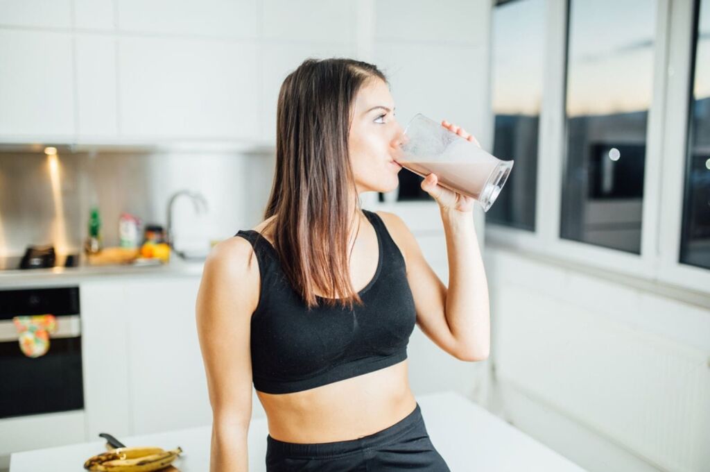 Mulher na cozinha bebendo um shake com whey protein