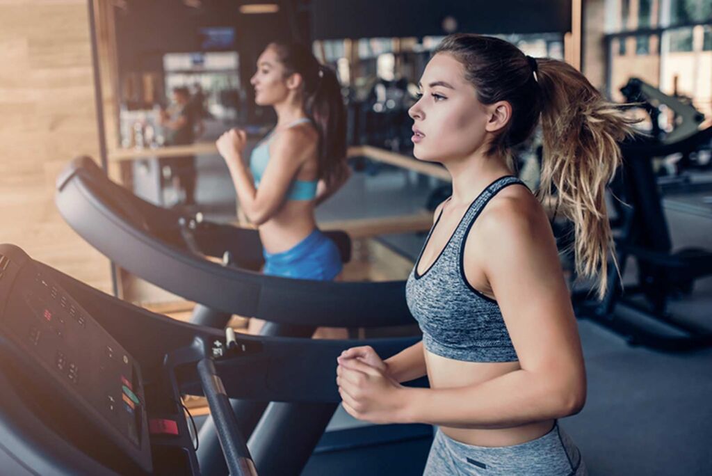 Duas mulheres correndo na esteira da academia