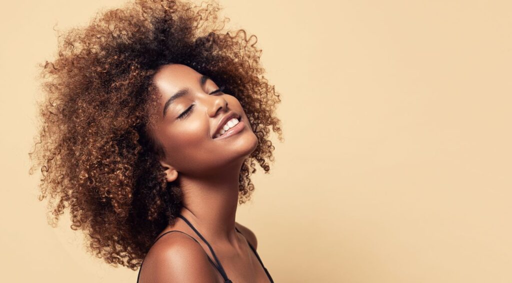 Mulher jovem, com cabelo afro, com os olhos fechados e sorrindo