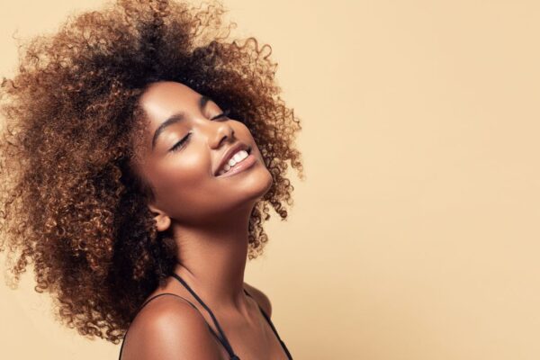 Mulher jovem, com cabelo afro, com os olhos fechados e sorrindo
