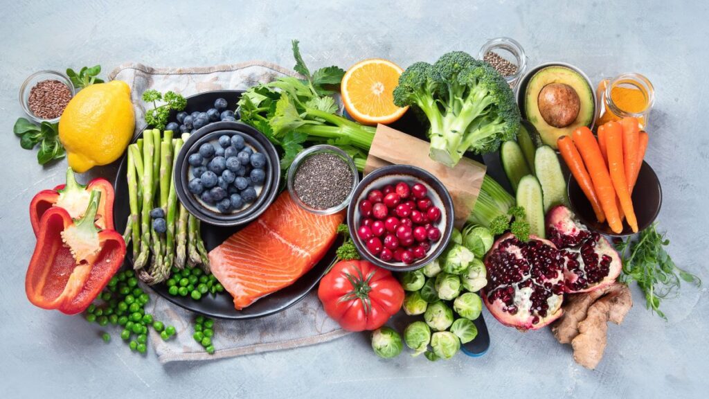 Mesa cheia de alimentos naturais ricos em antioxidantes, como brócolis, pimentão, cenoura, laranka, etc