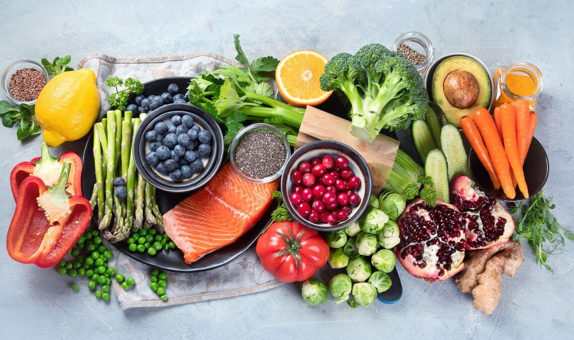 Mesa cheia de alimentos naturais ricos em antioxidantes, como brócolis, pimentão, cenoura, laranka, etc