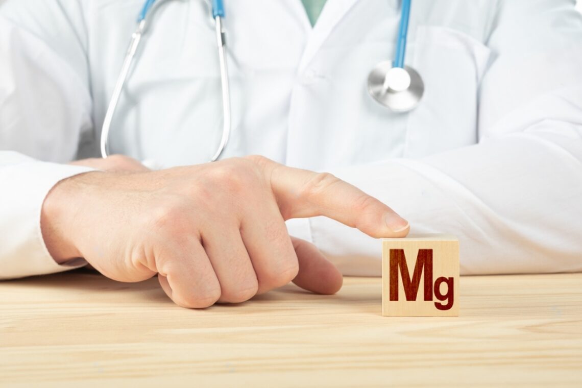Médico apontando para um quadradinho de madeira no qual está escrito as siglas "Mg"