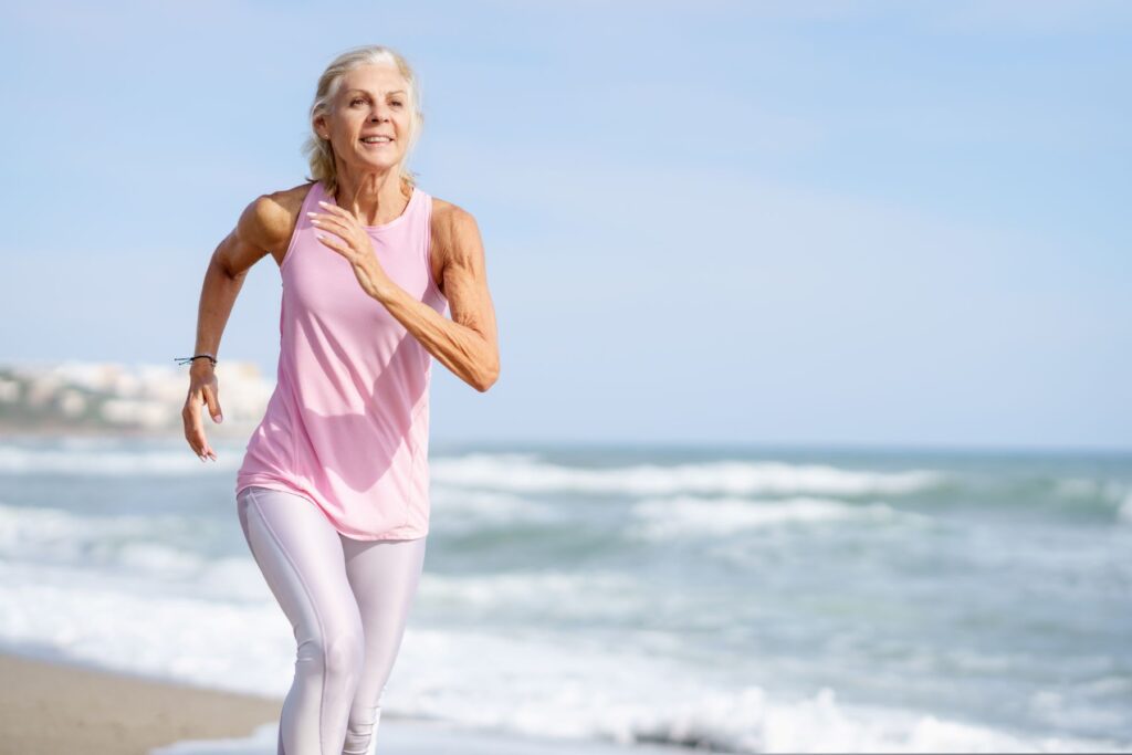 Mulher de meia idade, sorrindo e correndo na beira da praia