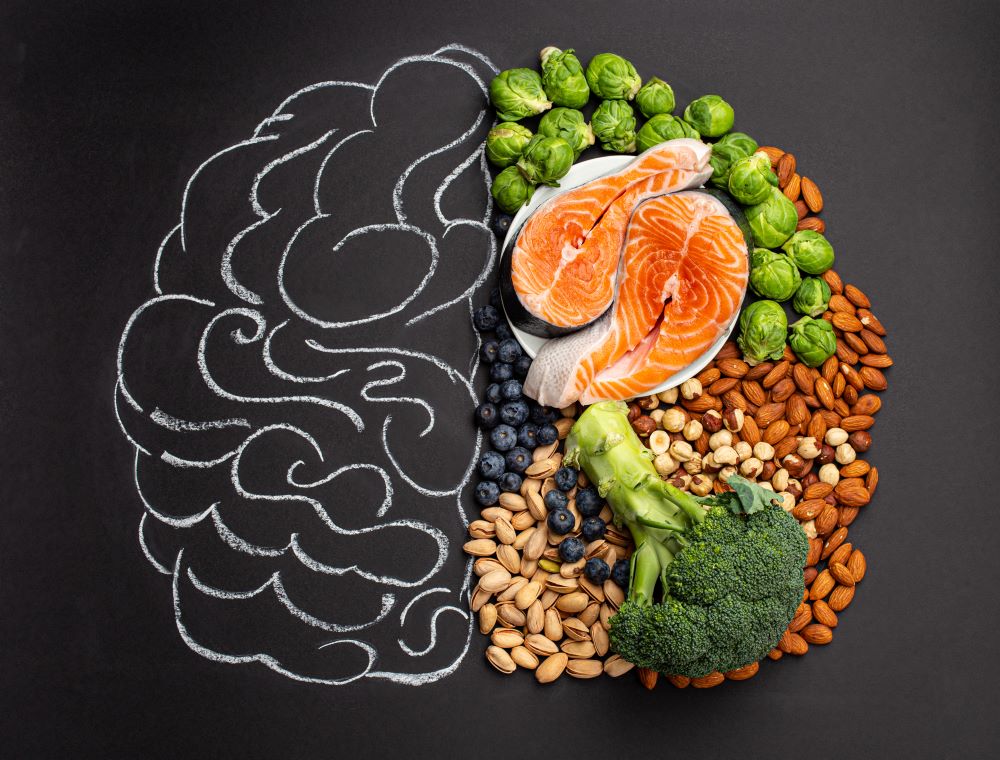 Imagem de um cérebro desenhado em giz e na metade do desenho há alimentos que fazem bem para a saúde cerebral