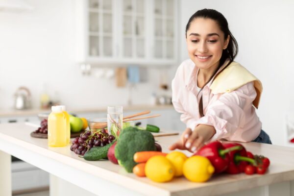 Mulher pegando um limão siciliano em cima de uma bancada com vários outros alimentos saudáveis