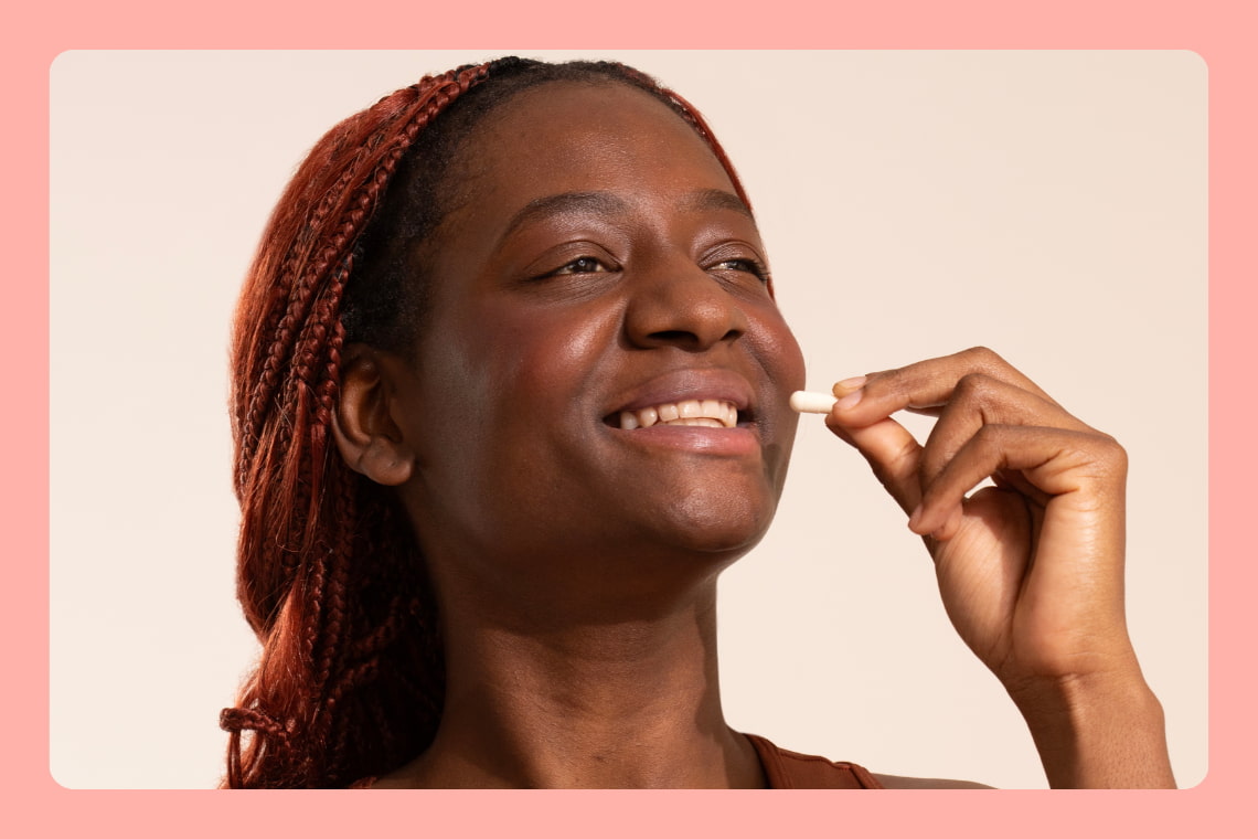 Mulher sorrindo prestes a tomar cápsula de resveratrol, em fundo claro.