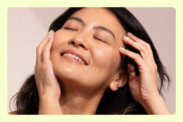 Mulher sorridente com olhos fechados toca o rosto, transmitindo bem-estar e autocuidado.