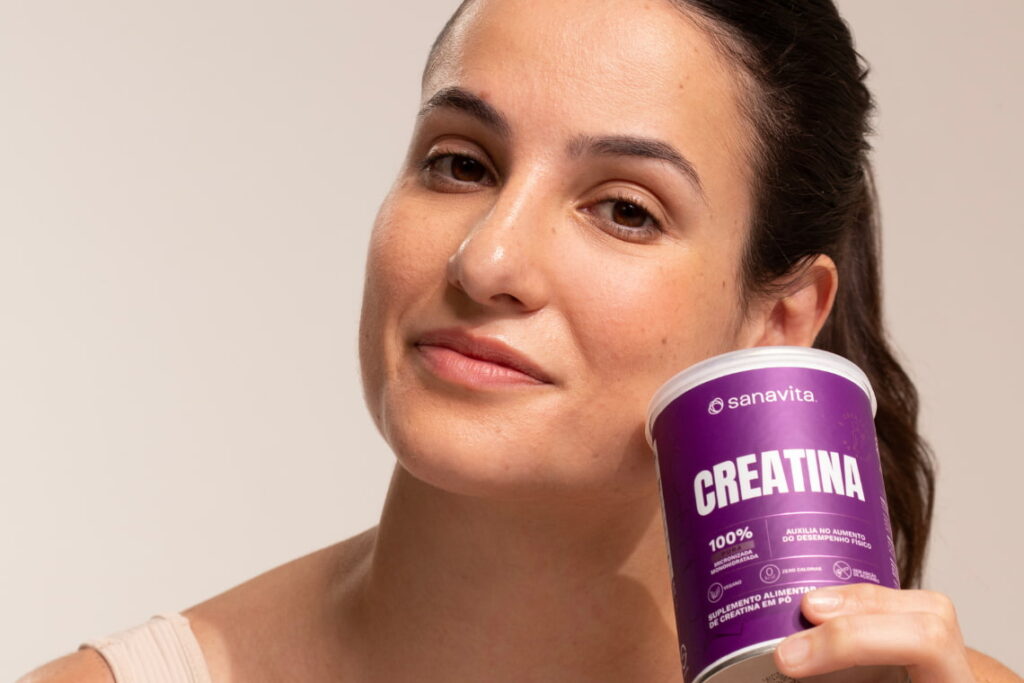 Mulher segurando embalagem roxa de creatina em pó Sanavita, destacando suplemento alimentar para desempenho físico.