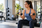Mulher fazendo treino de força com halteres em academia, com caneta de GLP-1 e garrafa de água ao lado.
